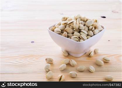 Pistachio nuts in a bowl placed on a wooden floor.
