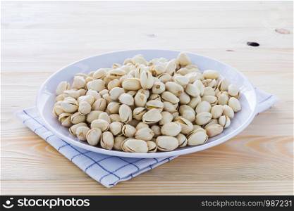 Pistachio nuts in a bowl placed on a wooden floor.