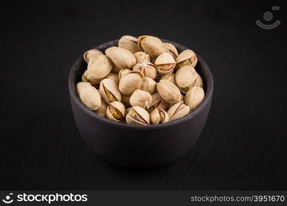 Pistachio nuts in stone bowl on dark background