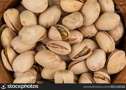 Pistachio nuts in wooden bowl on dark background