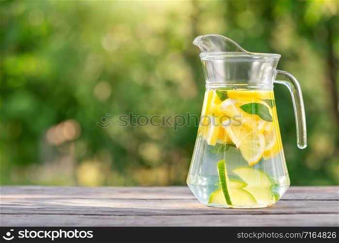 Pitcher of homemade lemonade on a wooden table. Green natural background. The bright summer sun. Organic food concept. Pitcher of homemade lemonade on wooden table