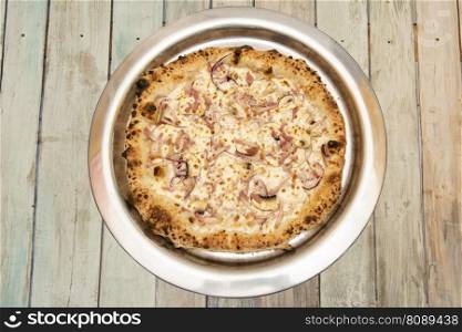 Pizza a la carbonara cooked in a stone oven with well-cooked edges, with guanciale, mushrooms and red onion on a metal tray