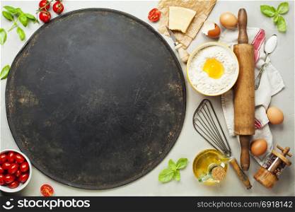 Pizza baking sheet and ingredients on rustic stone background. Top view copy space.