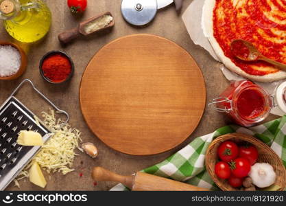 Pizza cutting board with ingredients at table. Dough for pizza on tabletop background. Recipe concept in kitchen