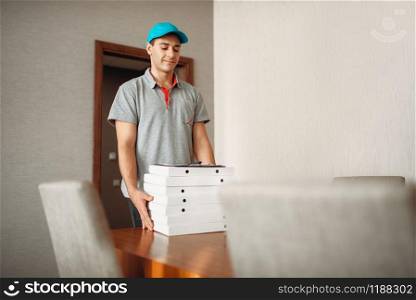 Pizza delivery boy leaves an order on the table, delivering service. Courier from pizzeria holds cardboard packages indoors
