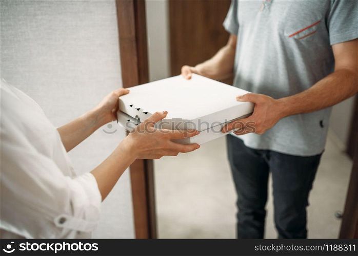 Pizza delivery man gives carton box to female client at the door, delivering service. Courier from pizzeria and woman indoors, takeaway deliver. Pizza delivery man gives box to female client