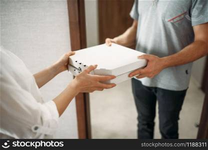 Pizza delivery man gives carton box to female client at the door, delivering service. Courier from pizzeria and woman indoors, takeaway deliver. Pizza delivery man gives box to female client