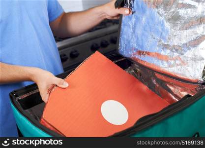 Pizza Delivery Person Putting Food Into Insulated Bag In Restaurant Kitchen