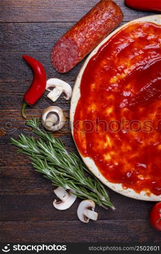 Pizza dough with sauce and different ingredients for cooking