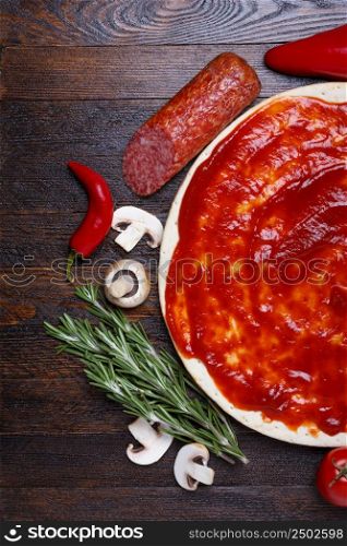 Pizza dough with sauce and different ingredients for cooking on wooden table