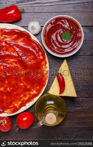 Pizza dough with sauce and different ingredients for cooking on wooden table