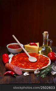 Pizza dough with tomato sauce during preparation, with a lot of ingredients on wooden table