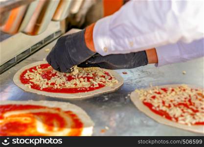 Pizza maker preparing a margherita pizza sprinkling diced mozzarella cheese on a pasta base already seasoned with tomato sauce and ready to bake. Italian cuisine.