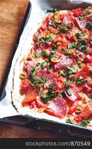 Pizza on tray topped with tomato, sauce, cheese, meat, vegetales, fruits and herbs
