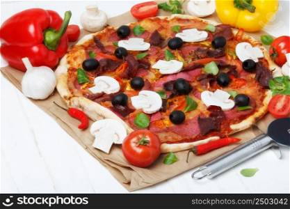 Pizza on white wooden table with tomato, ham, mushrroms, pepper, garlic and olives