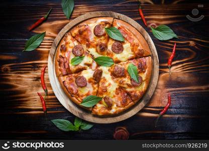 Pizza on wooden tray and chilli basil leaf top view / delicious tasty fast food italian traditional pizza cheese with Mozzarella , Smoked pork sausage , Pineapple ham on topping sauce
