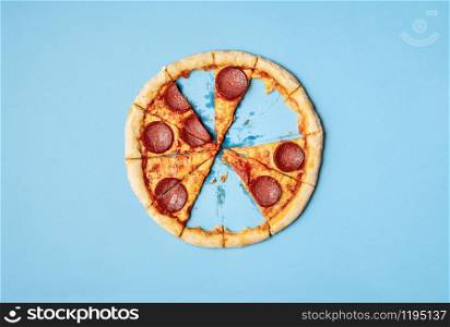 Pizza pepperoni slices and leftover crust on blue background. Above view of sliced pizza salami with missing slices and crust leftover. Eating pizza.