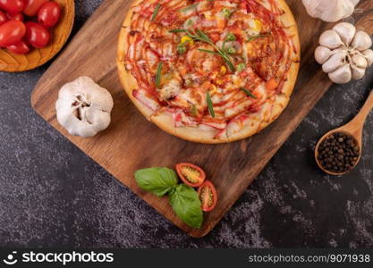Pizza placed on a wooden plate complete with pepper seeds. Tomatoes and garlic. Top view.