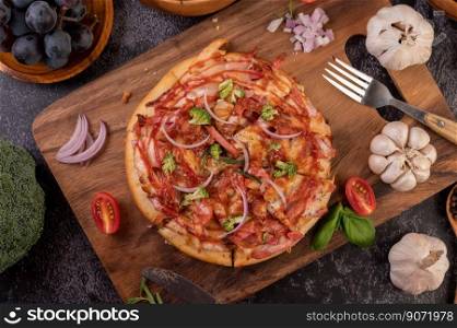 Pizza placed on a wooden plate complete with pepper seeds. Tomatoes and garlic.  Top view.