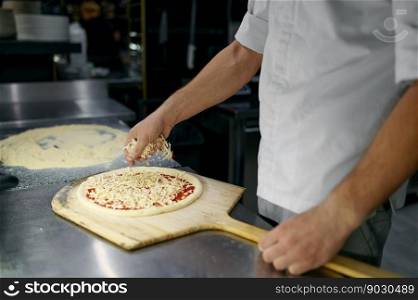 Pizza preparation process concept. Closeup chef hands sprinkling cheese over fresh pizza-baze. Pizza preparation process with closeup chef hands sprinkling cheese