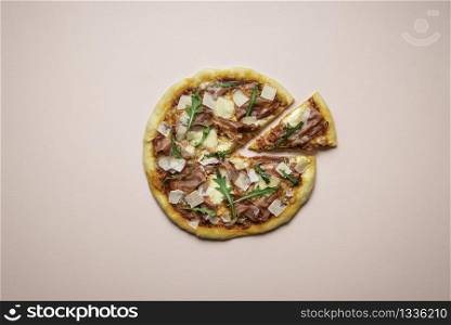 Pizza prosciutto with arugula and one cut slice on pink background. Sliced ham pizza top view. Italian traditional dinner.