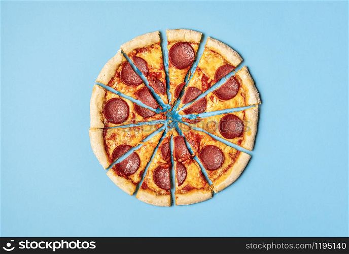 Pizza salami cut in slices isolated on a blue background. Above view of sliced pizza pepperoni. Divided pizza in portions. Famous food. Greasy dish.