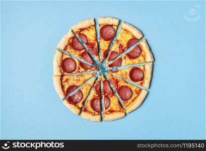 Pizza salami cut in slices isolated on a blue background. Above view of sliced pizza pepperoni. Divided pizza in portions. Famous food. Greasy dish.
