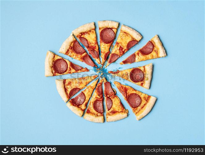 Pizza salami cut in slices on a blue background. Above view of sliced pizza pepperoni. Ready to eat pizza. Fast food. Unhealthy food. Tasty pizza.