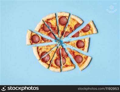 Pizza salami cut in slices on a blue background. Above view of sliced pizza pepperoni. Ready to eat pizza. Fast food. Unhealthy food. Tasty pizza.