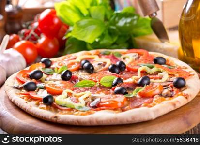 pizza with bacon, vegetables and olives on wooden table