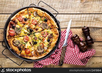 pizza with cheese, tomatoes, mushrooms, ham, sausage and olives on a wooden table, top view