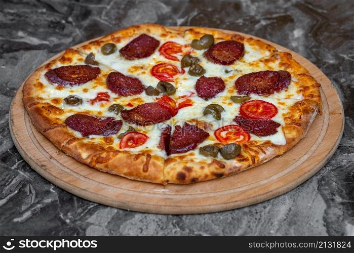 Pizza with green olives, Turkish sausage and cheese on a cutting board