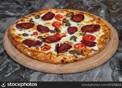 Pizza with green olives, Turkish sausage and cheese on a cutting board