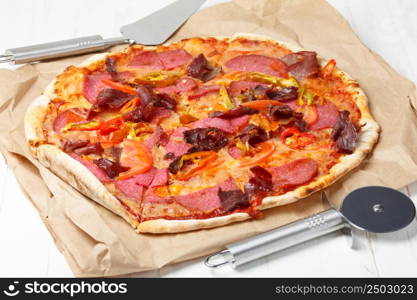 Pizza with ham, salami and chili pepper, on wooden table with lifter and cutter knife