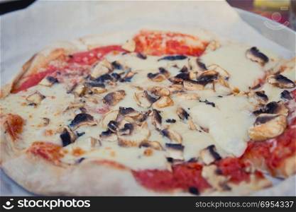 Pizza with mushrooms on a baking paper.