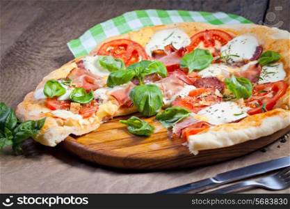 Pizza with prosciutto, mozzarella, tomatoes and basil, selective focus