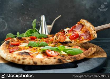 Pizza with salami and tomatoes on black wooden table, someone taking one piece. Pizza with salami and tomatoes