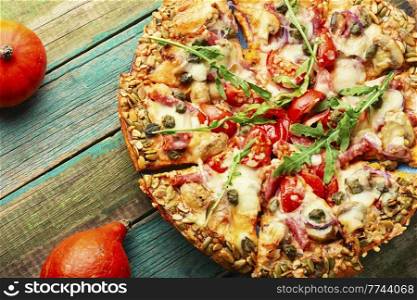 Pizza with salami, cheese, tomato on a pumpkin flatbread. Autumn recipe. Pumpkin-based pizza, wooden table