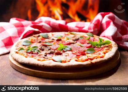 pizza with salami, ham and vegetables on wooden table