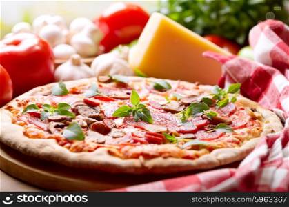 pizza with salami, ham and vegetables on wooden table