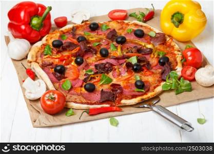 Pizza with salami, olives, ham, chili pepper and cheese on wooden table with pizza lifter still life
