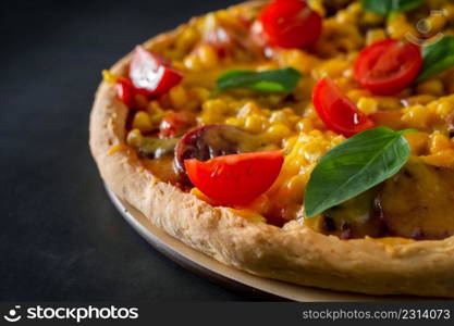 Pizza with tomatoes and basil close-up. Tasty italian pizza with tomatoes, cheese and basil close-up on a black background. Slice of pizza with corn and cheese on a dark background. Vertical photo, place for text.. Pizza with tomatoes and basil close-up
