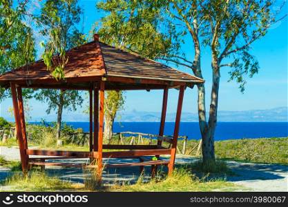 Place to relax for tourists in Greece. Benches under wooden shelter near sea, nature leisure spot.. Benches under shelter in Greece near sea