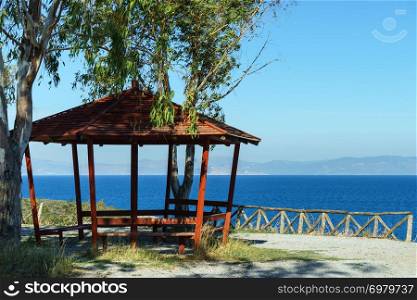 Place to relax for tourists in Greece. Benches under wooden shelter near sea, nature leisure spot.. Benches under shelter in Greece near sea