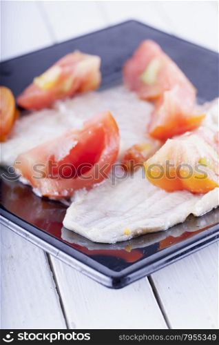 Plaice with tomatoes over black reflecting plate, horizontal image