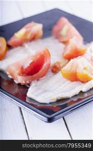 Plaice with tomatoes over black reflecting plate, horizontal image