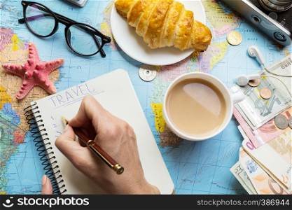 Plan of trip. Women's hands and notepad for writing ideas, map, retro camera, money, coins, croissant, coffee, pen, sunglasses, smartphone