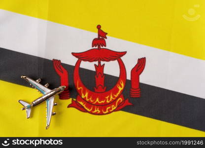 Plane over the flag of Brunei Darussalam travel concept. Toy plane on a flag in the background.. Plane over the flag of Brunei Darussalam travel concept.