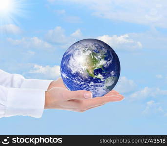 Planet Earth in the female hand against the sky