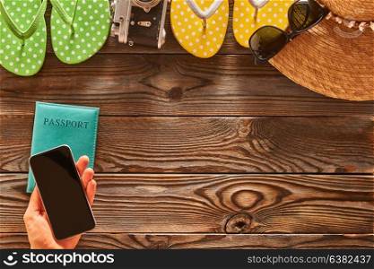 Planning a beach trip. Woman holding smartphone. Travel items for beach tourism still life over wooden background.